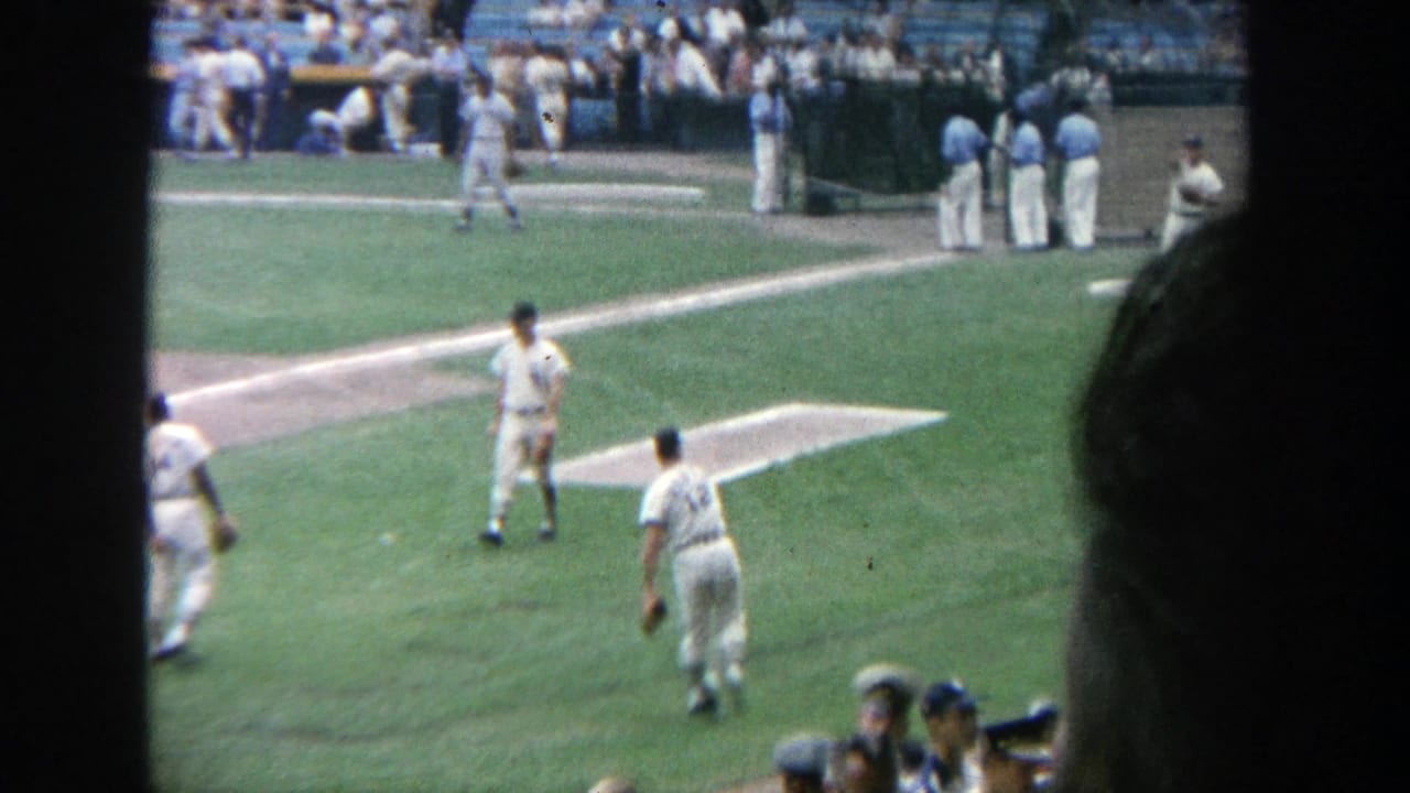 Baseball players on the infield seen from stadium seats, with spectators in the stands behind them.
