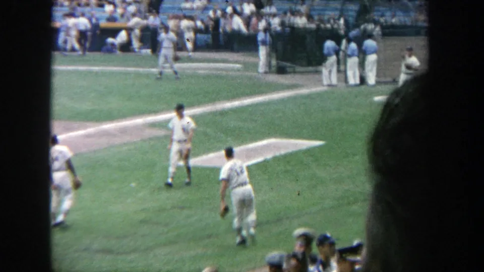 1964 Yankee Stadium home-movie view of baseball players on the infield, partly obscured by dark foreground shapes.