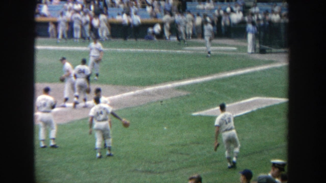1964 Yankee Stadium home-movie frame with players moving across the infield and a busy spectator background.