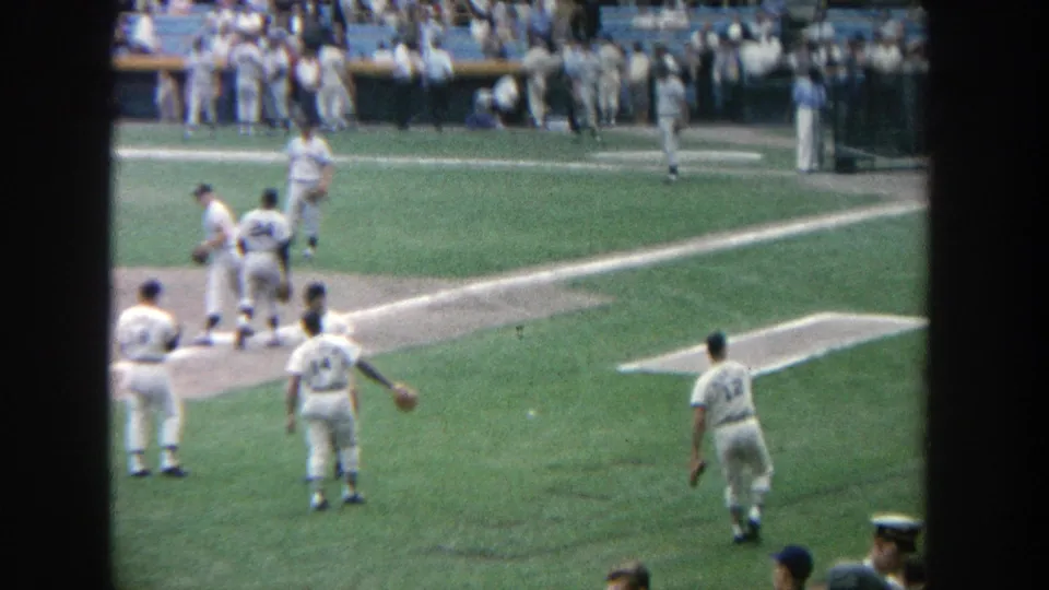 1964 Yankee Stadium home-movie frame with players moving across the infield and a busy spectator background.
