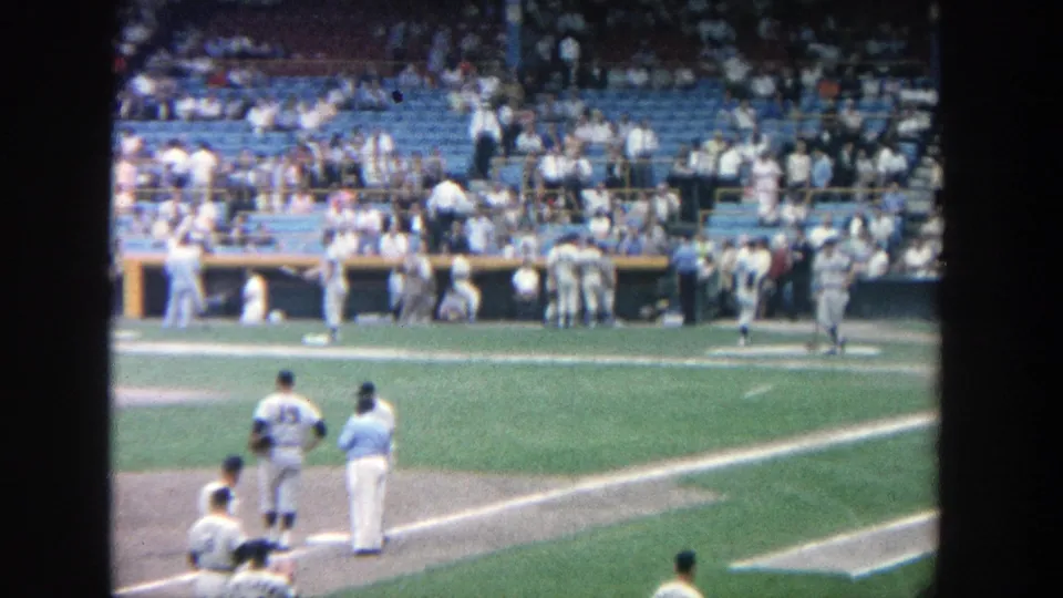 1964 Yankee Stadium frame with players near the first-base side and a busy dugout and seating area behind them.