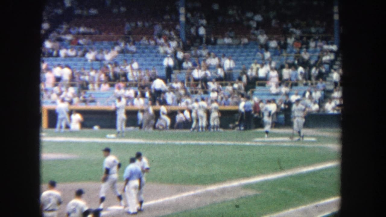 Handheld 8mm view of Yankee Stadium in 1964, with players near the infield and a crowded seating section beyond the dugout.