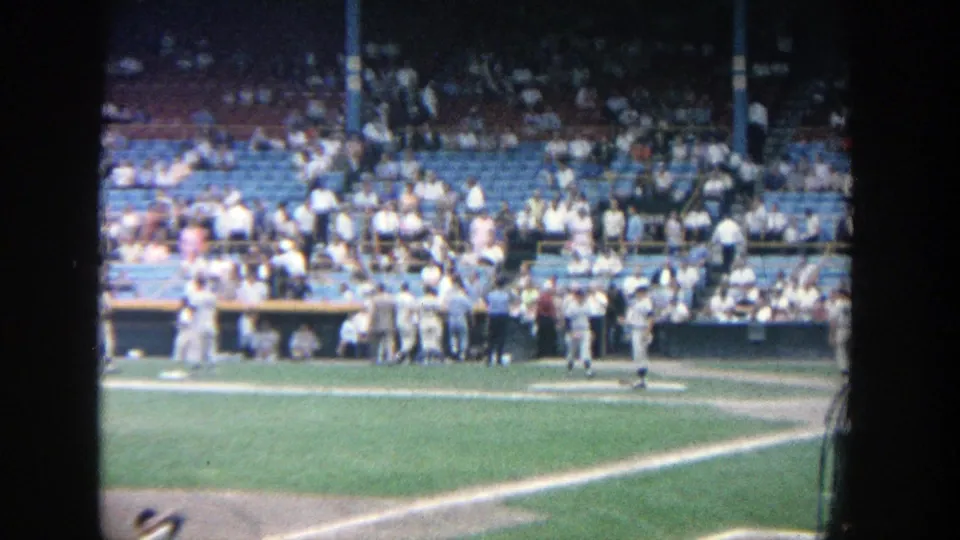 Soft 8mm view of a 1964 baseball game at Yankee Stadium, with players by the dugout and fans across the stands.