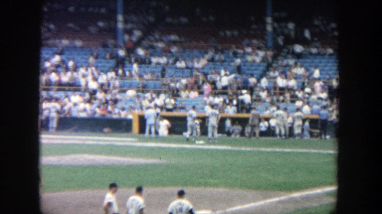 Baseball field and blue stadium seats with spectators and players visible from the stands.