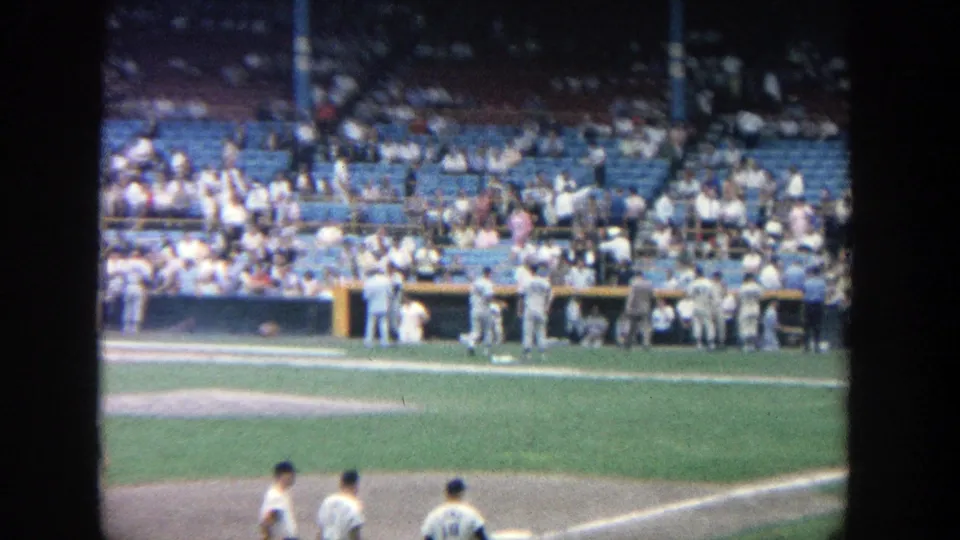 1964 Yankee Stadium home-movie view of players near the field and spectators in blue seats after a baseball game.