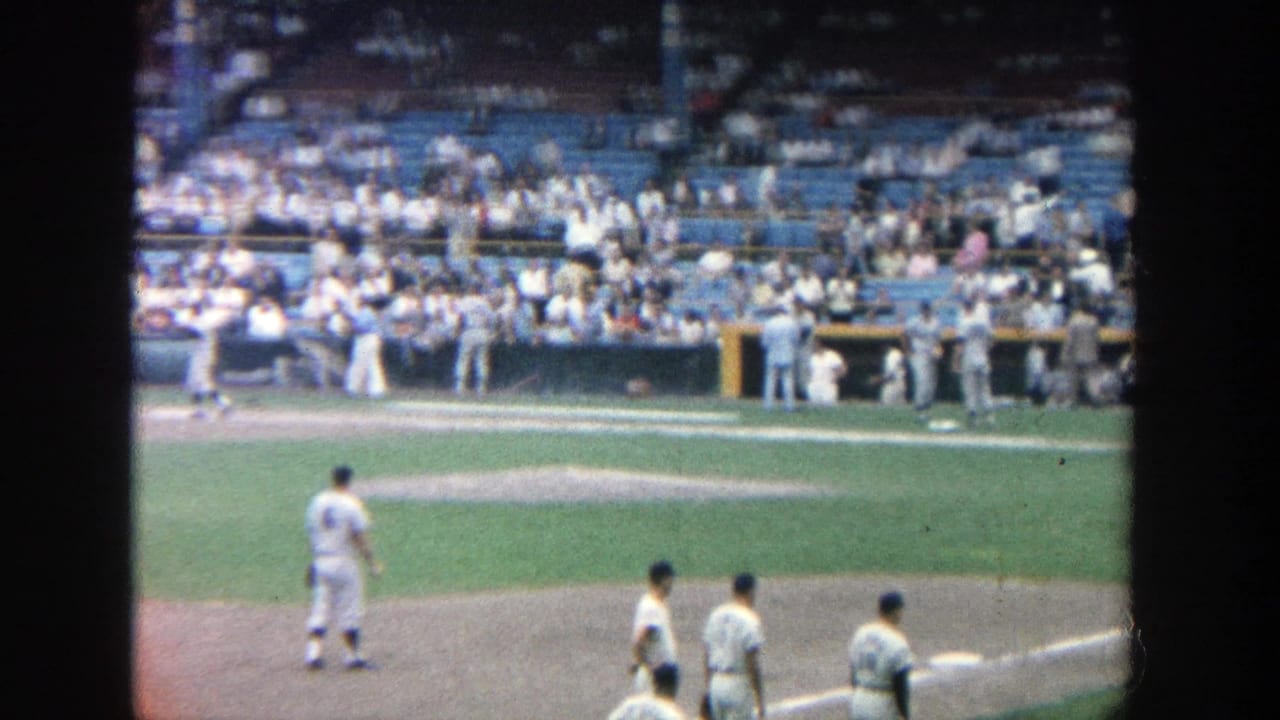 Yankee Stadium view from the stands showing players on the field and spectators seated behind them in 1964 footage.