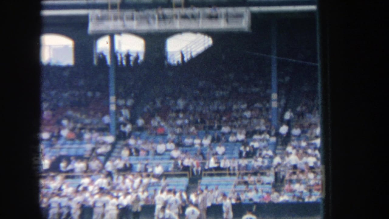 Visitor-shot 8mm view of Yankee Stadium seating, with shaded upper stands and spectators in blue seats.