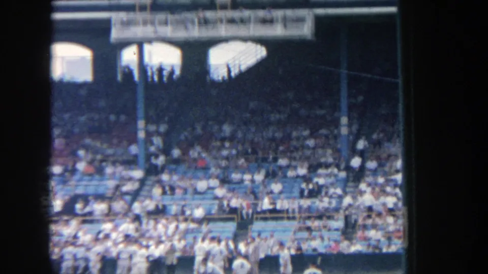 Visitor-shot 8mm view of Yankee Stadium seating, with shaded upper stands and spectators in blue seats.