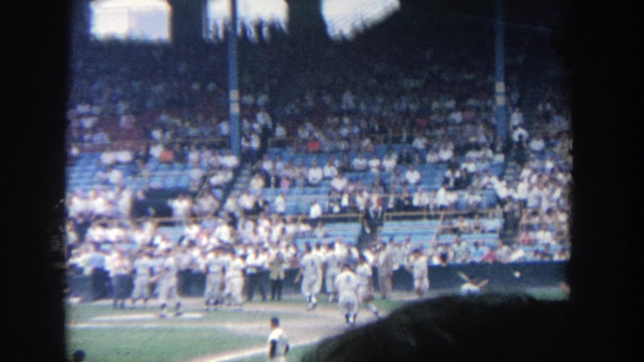 Postgame Yankee Stadium scene with fans in blue seats and players near the field in 1964 home-movie footage.