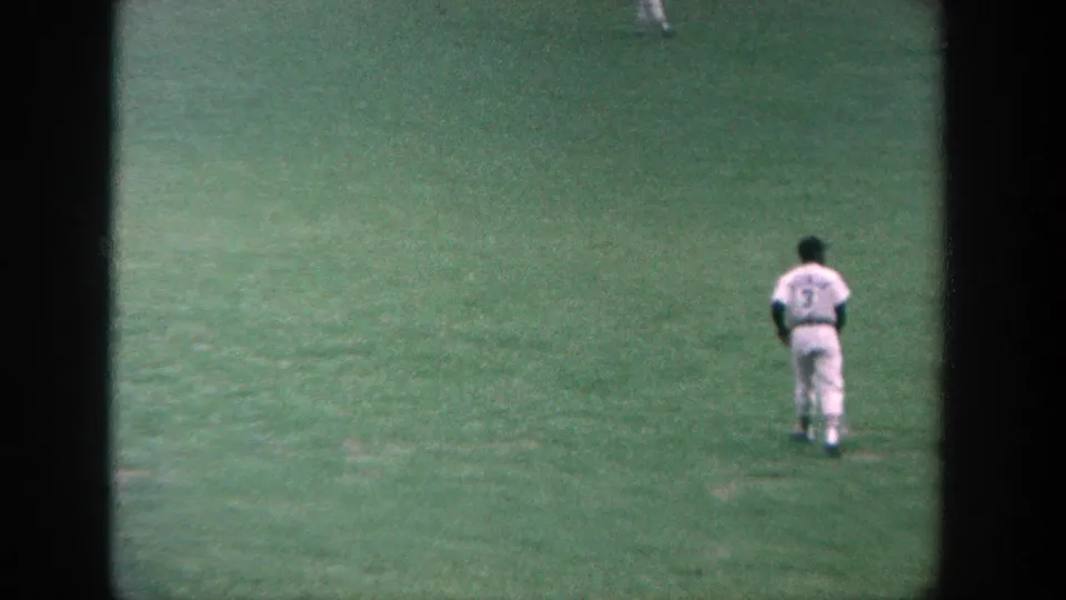 1964 Yankee Stadium home-movie frame with a distant player standing in the outfield during warm-up.
