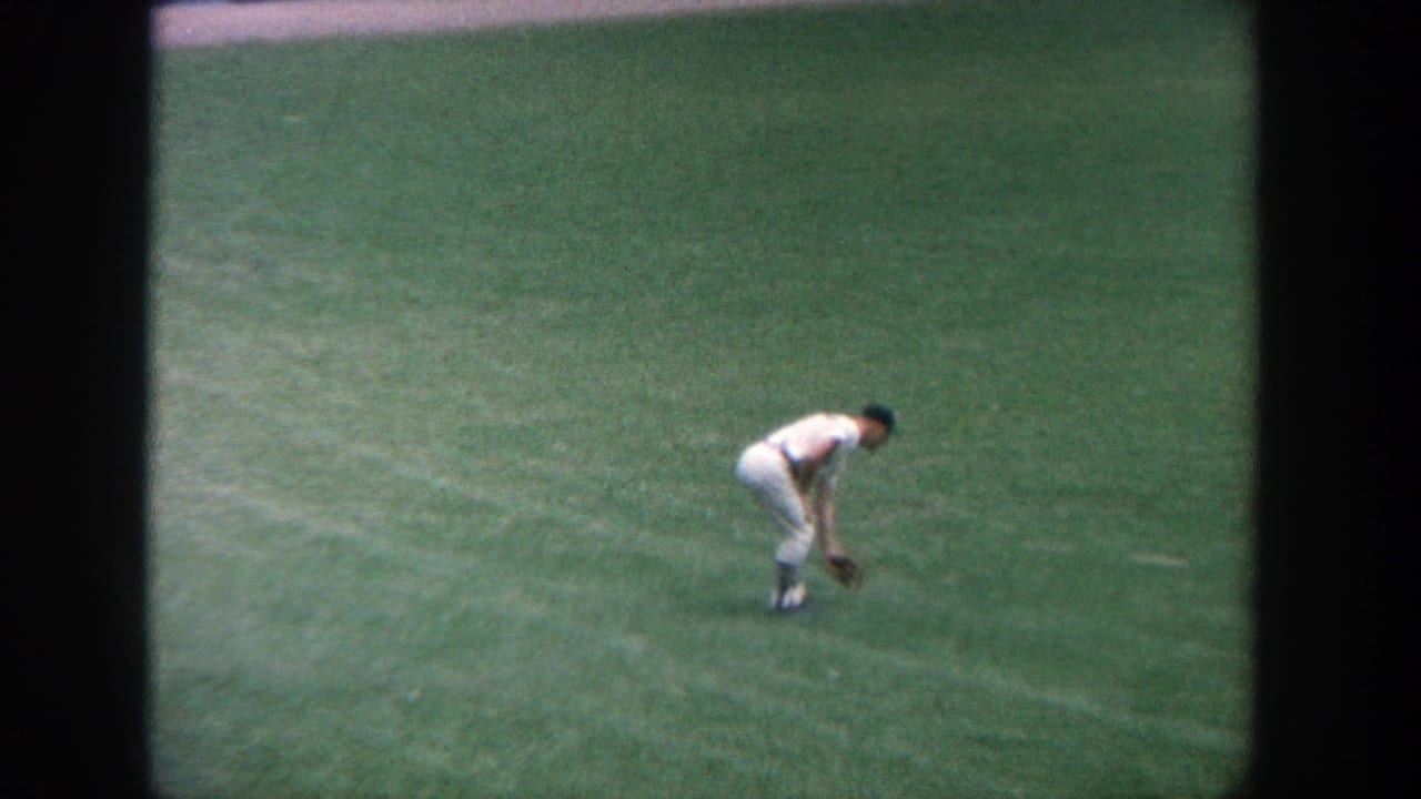 Baseball player in a white uniform bends on green outfield grass.