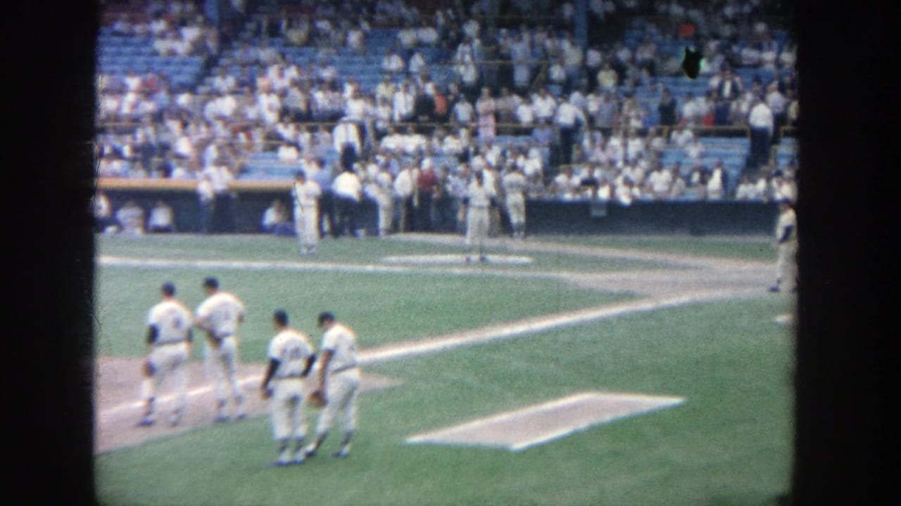 Several baseball players walk and stand near the baseline with spectators in the background.
