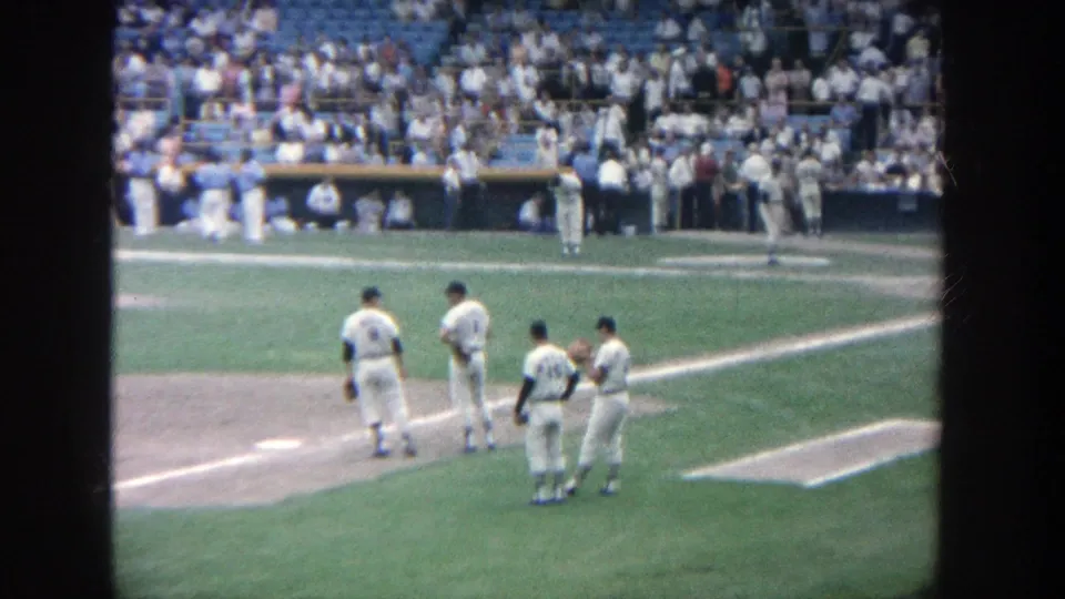 Home-movie view at Yankee Stadium in 1964 showing four players standing together on the infield near the foul line.