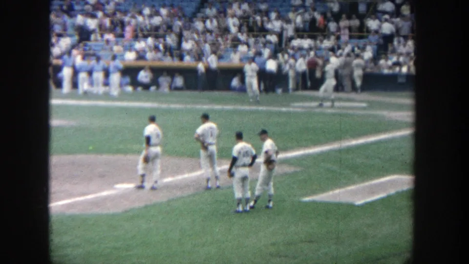 1964 Yankee Stadium frame showing players spaced near the infield, with the dugout and crowded stands beyond.