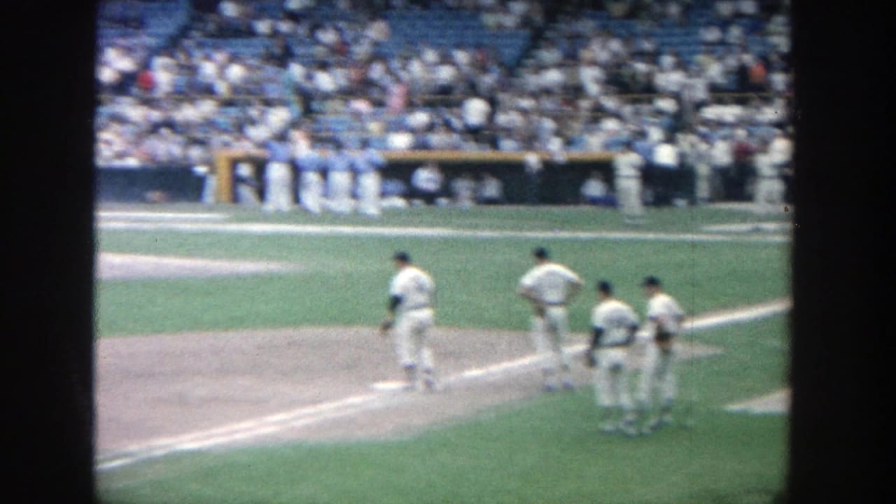 1964 8mm view of baseball players near the infield at Yankee Stadium, with blue bleachers and spectators in the background.