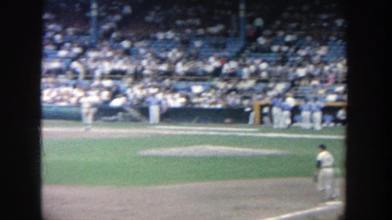 Wide stadium view with a player on the field and spectators seated behind the dugout.
