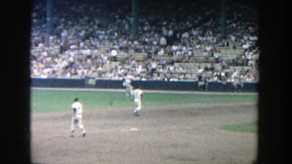 1964 Yankee Stadium frame showing an infield throw during a live baseball game, with a crowded seating section behind.
