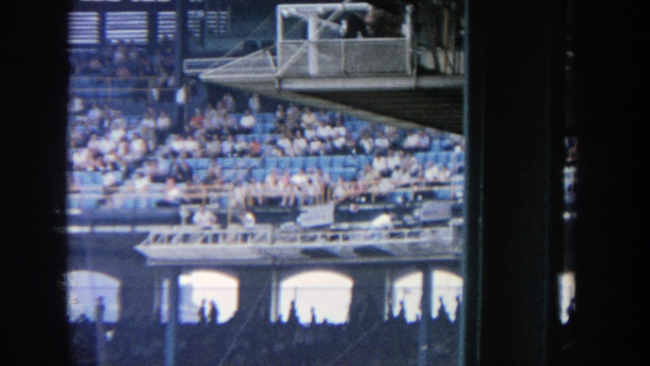 Crowded grandstand with blue seats and a small elevated box area.