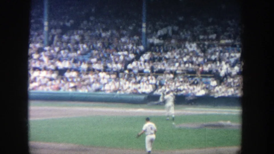 Baseball field at Yankee Stadium in 1964, with players in white uniforms in front of a crowded grandstand.