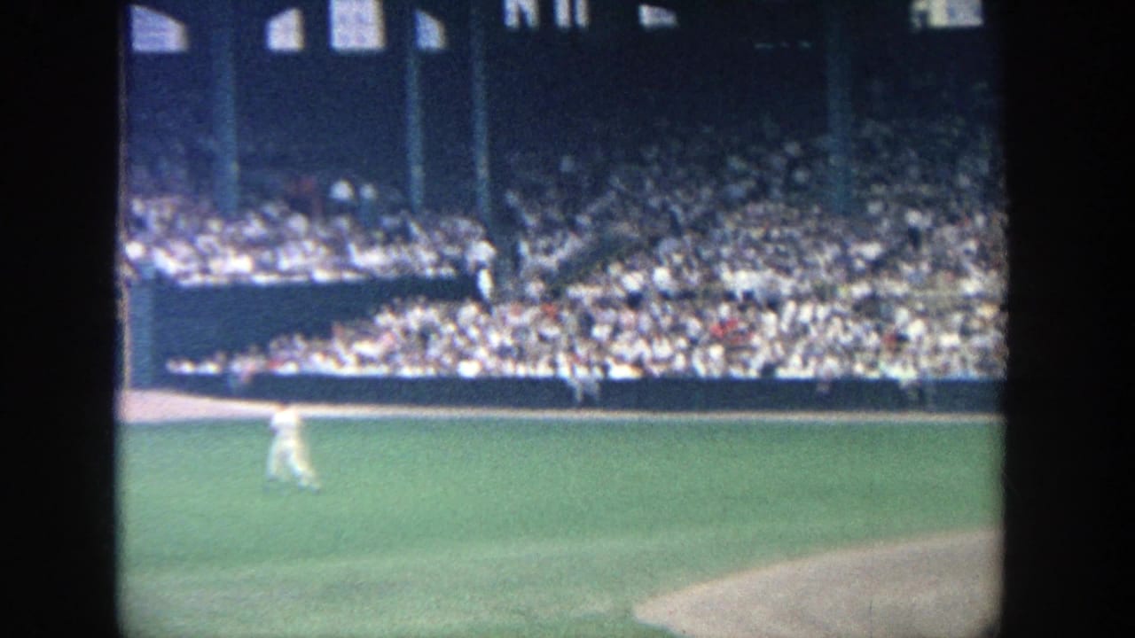 Yankee Stadium field view with green outfield grass, partial infield dirt and spectators seated beneath stadium structure.