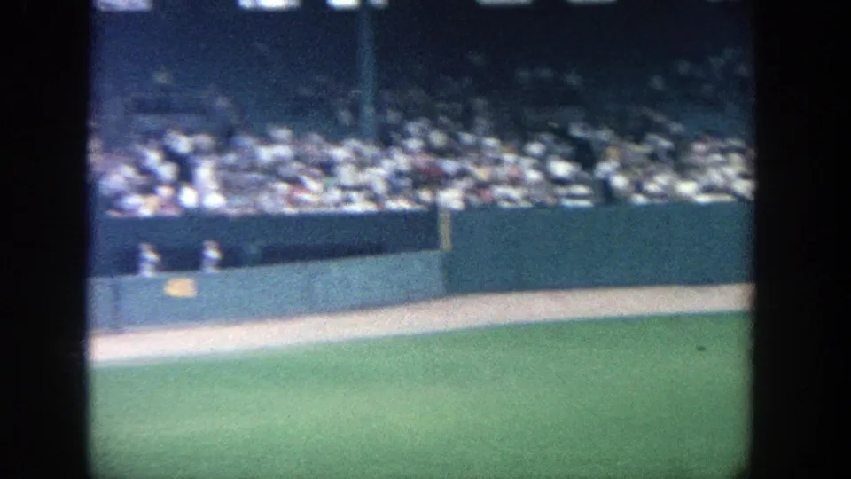 1964 Yankee Stadium frame looking across the warning track and outfield wall toward packed spectator seating.