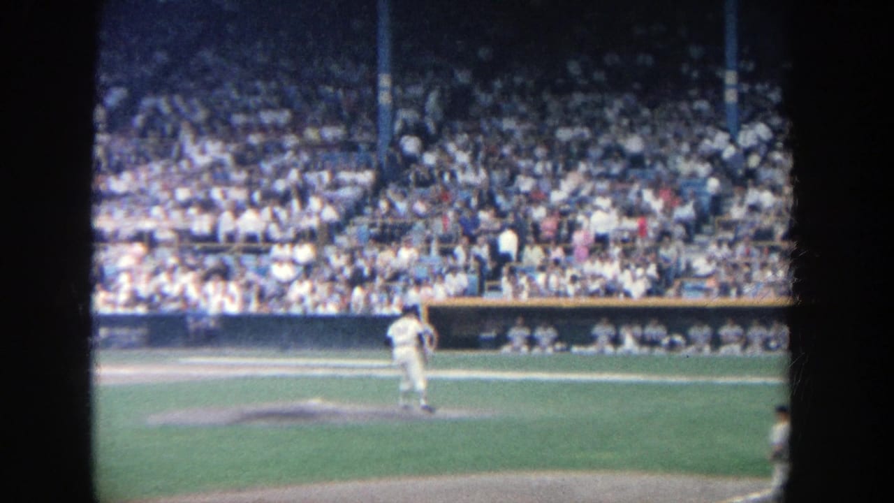 Pitcher stands on the mound as spectators fill the stadium seating.
