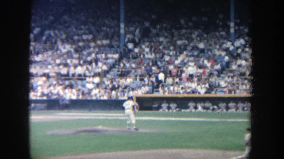 Spectator-shot 8mm frame at Yankee Stadium with the pitcher centered on the mound and the crowd visible across the stands.