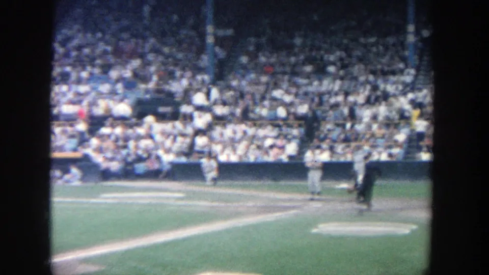 1964 Yankee Stadium view toward home plate, with catcher and umpire near the plate and spectators filling the background.