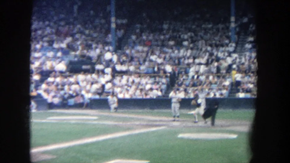 8mm frame from Yankee Stadium showing the catcher and umpire near home plate as the crowd watches from the stands.