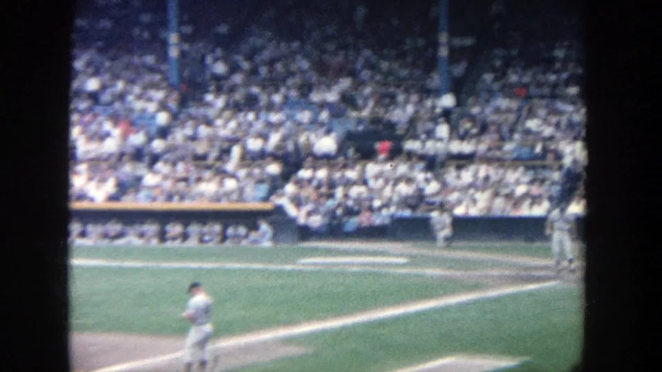 1964 Yankee Stadium view from the stands with a player moving across the infield and a crowded seating section beyond.