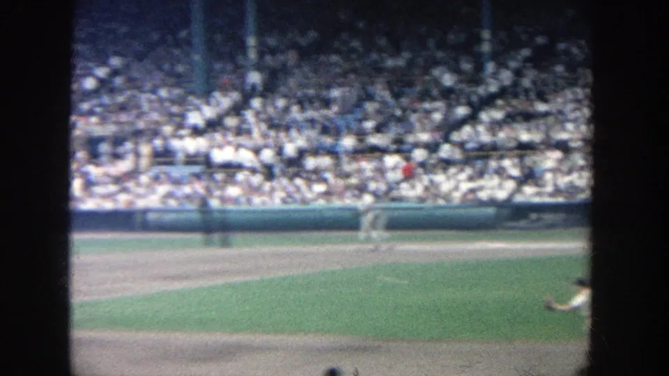 Wide 1964 Yankee Stadium home-movie view of the field and stands, with a player partly visible at the lower right.