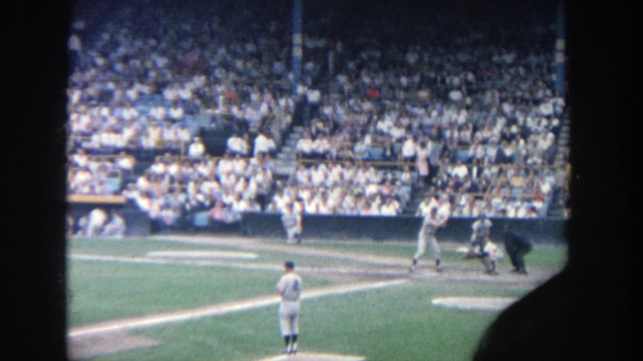 Batter at home plate with catcher, umpire, nearby players, and packed stands.