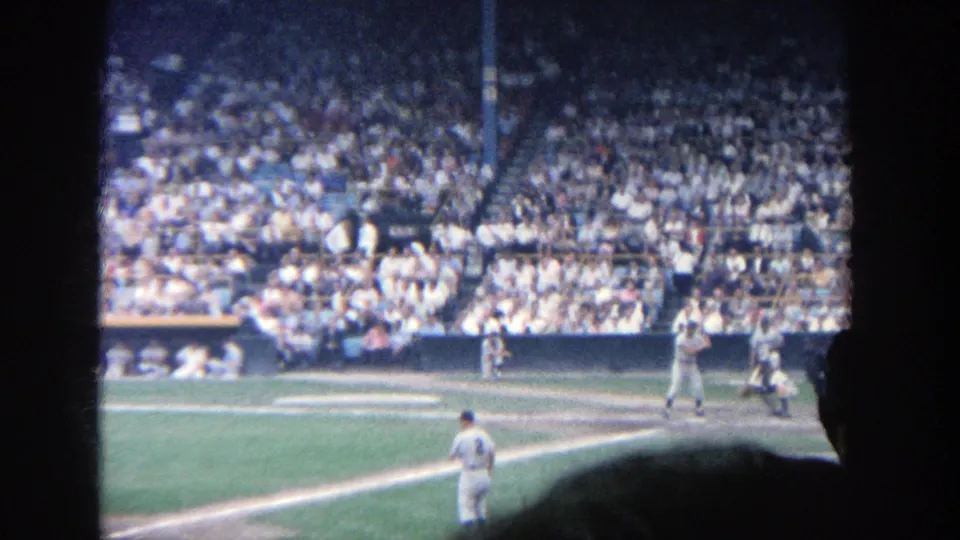 Spectator-shot 1964 Yankee Stadium view of the batter's box, pitcher, home plate area, and crowded seating.