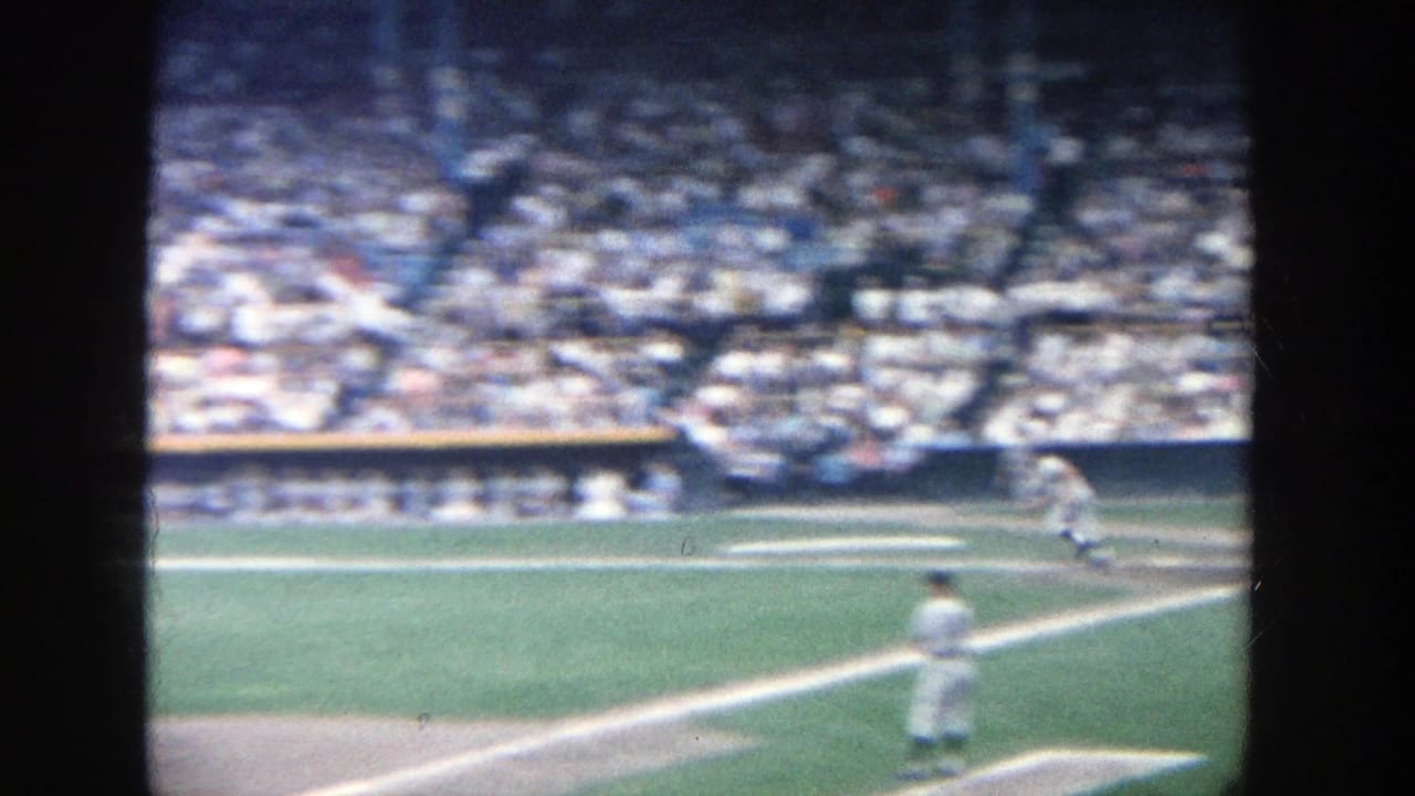 Baseball field seen from the stands with players, infield lines, and a packed crowd.