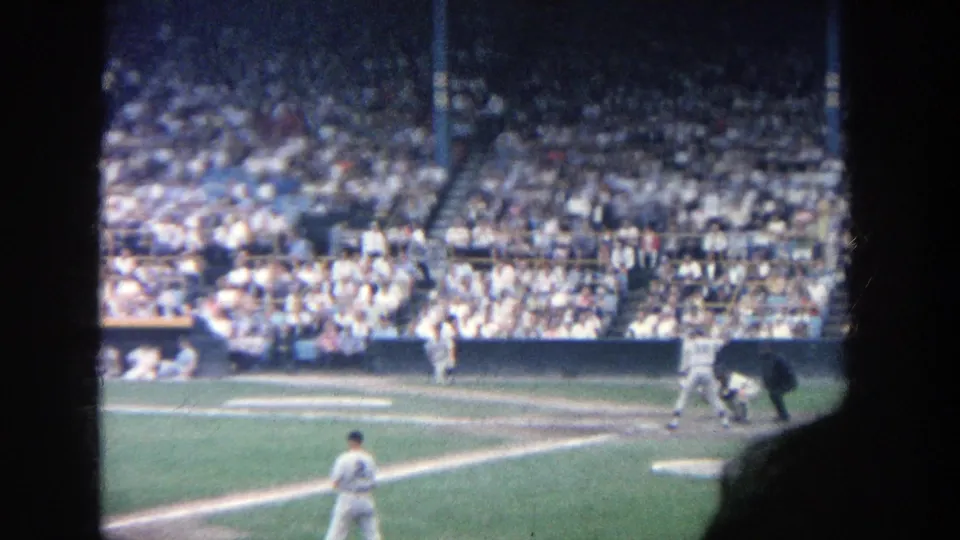 Handheld 8mm view of a 1964 Yankee Stadium baseball moment near home plate with the crowd beyond.