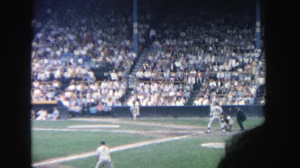 Spectator-shot 1964 Yankee Stadium baseball frame showing pitcher, batter area, umpire, and crowded stands.