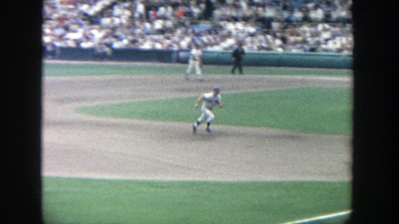 1964 Yankee Stadium home-movie frame showing a baseball player running on the infield as spectators fill the background stands.