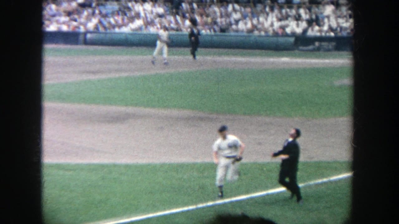 Player near the foul line with an umpire or official nearby and spectators in the stands.