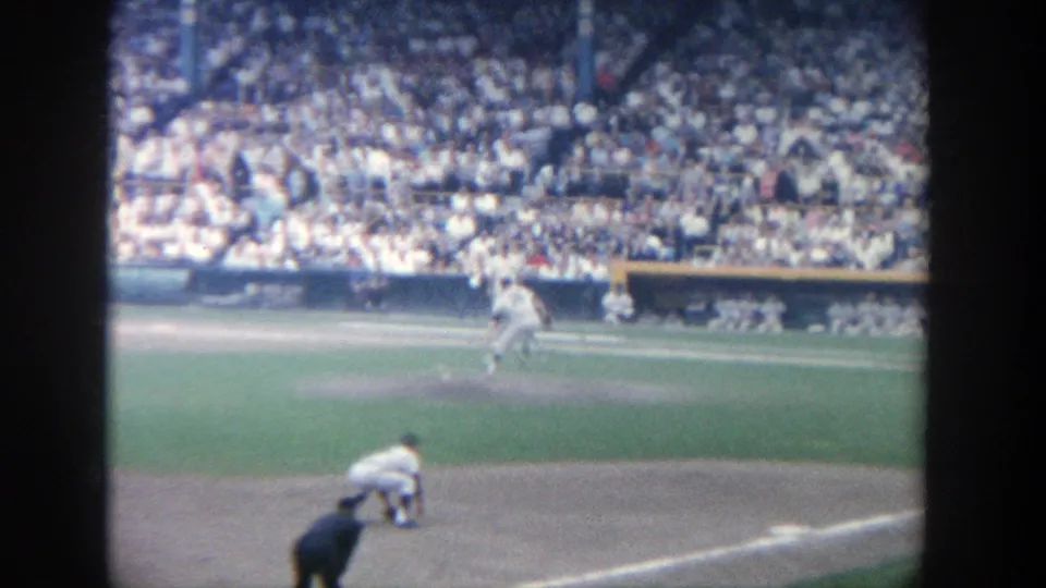 From the stands at Yankee Stadium in 1964, the frame shows live baseball action with players positioned near the mound and home plate area.