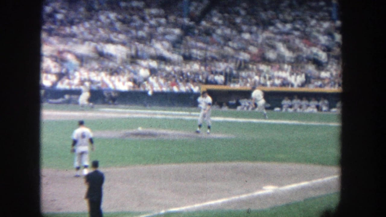 Baseball action near home plate with players on the field and a large crowd in the stands.