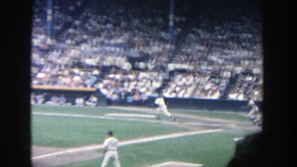 1964 Yankee Stadium frame showing a batter or runner leaving the plate area toward first base as players and the crowd remain visible.