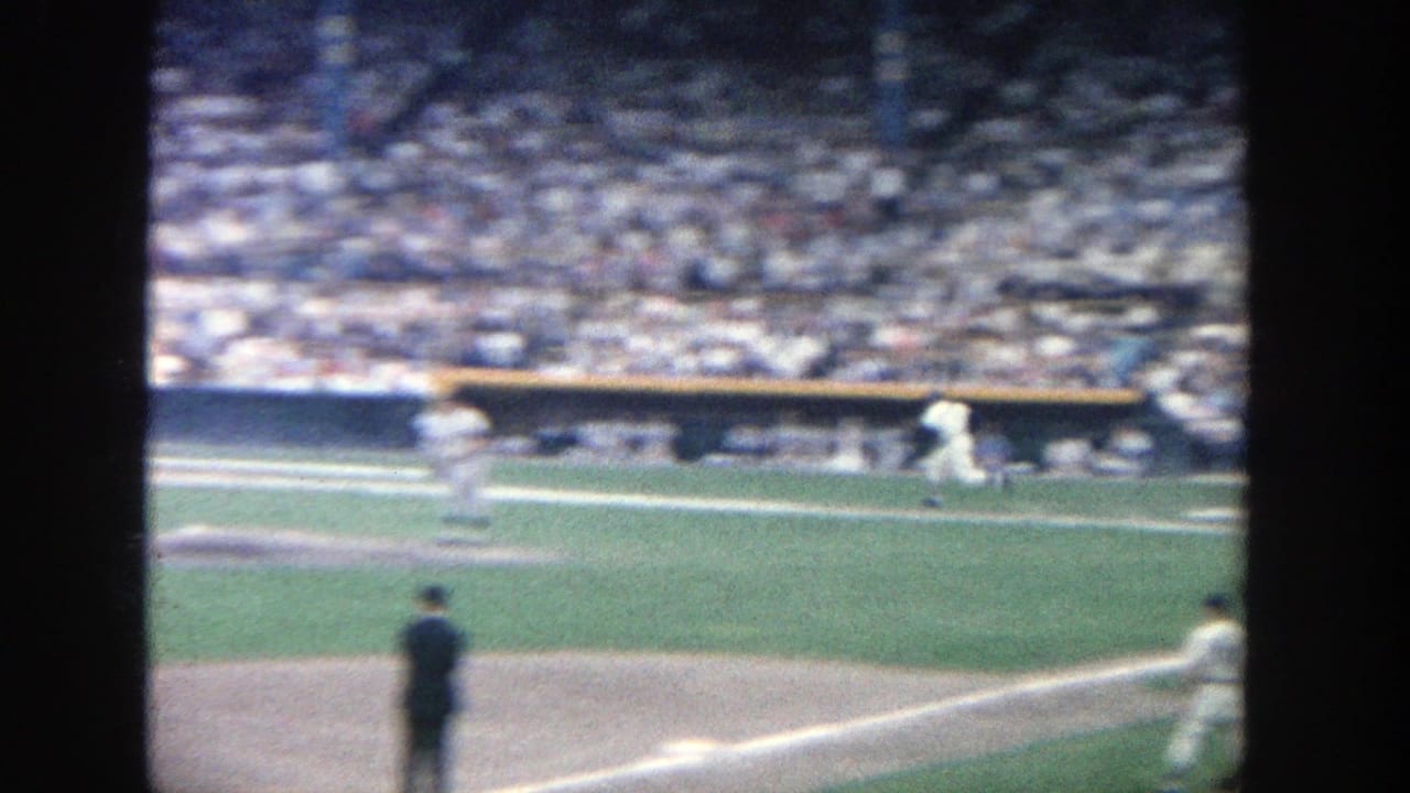 1964 Yankee Stadium home-movie frame showing players on the field with packed grandstands in the background.