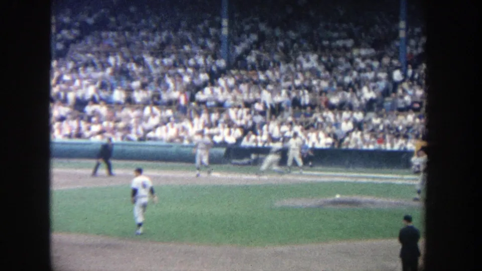 Distant 1964 Yankee Stadium view of players and an umpire during a baseball game before crowded stands.