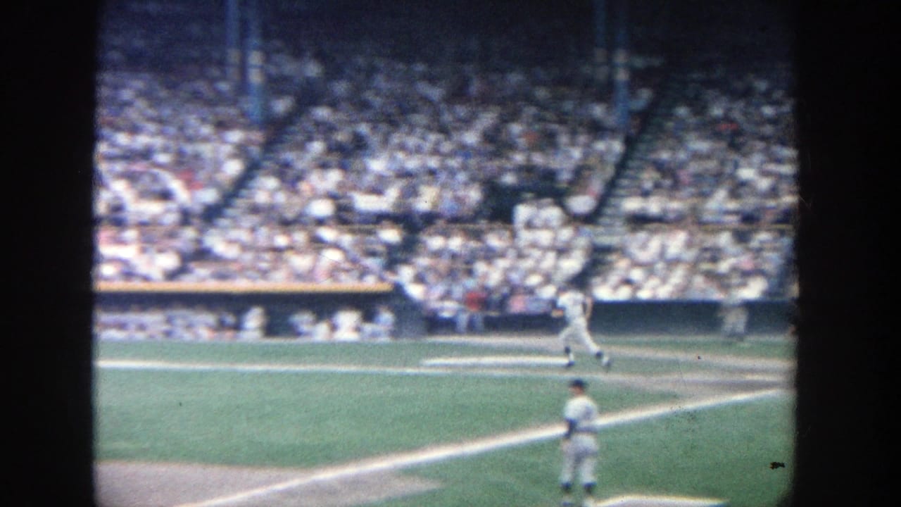 Visitor-shot 1964 Yankee Stadium view with crowded seating, bright field grass, and players spread across the diamond.