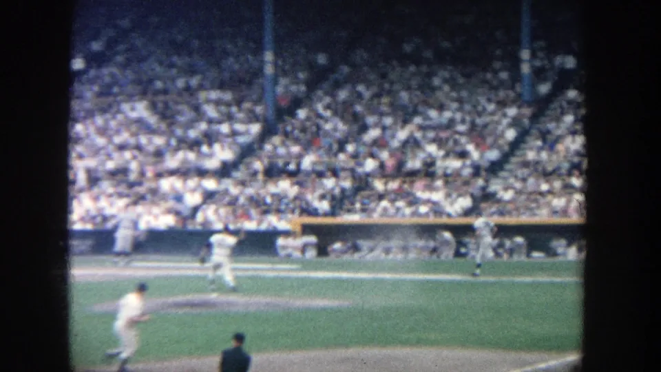 1964 Yankee Stadium frame showing a pitcher in motion, batter near home plate, and spectators filling the grandstand.