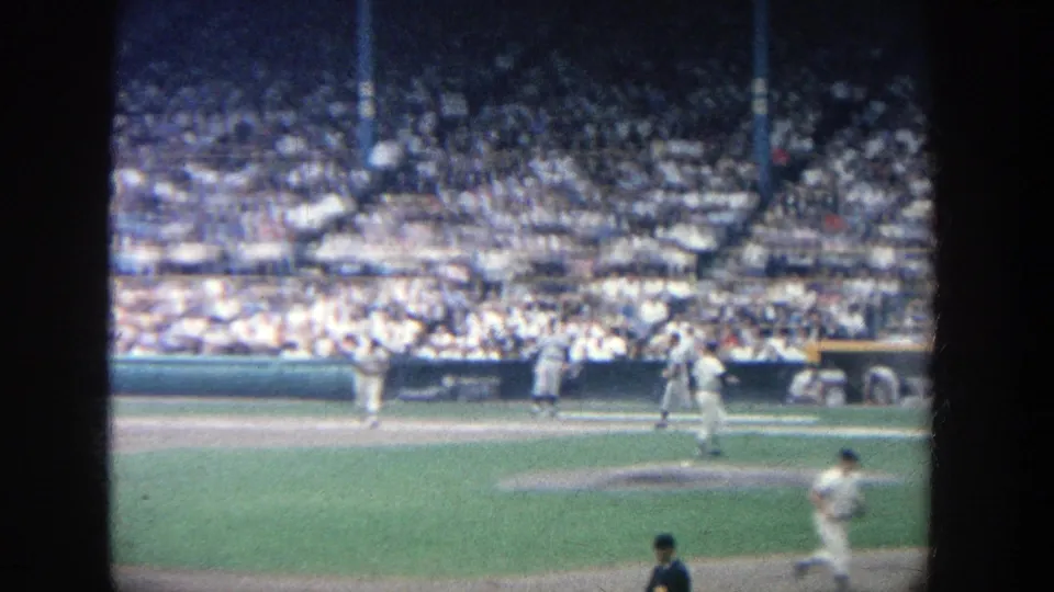 Home-movie view at Yankee Stadium in 1964 with on-field baseball action framed against a dense crowd in daylight.
