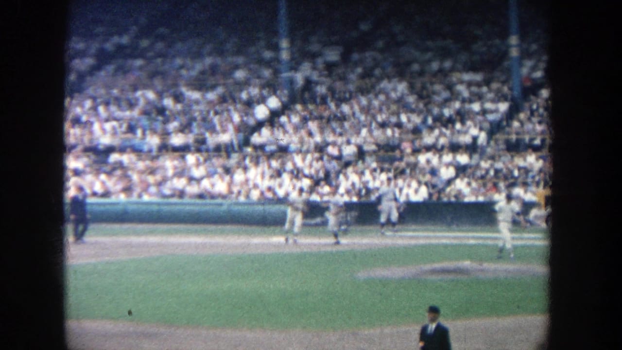 Baseball players and an official on the field before a crowded stadium section.