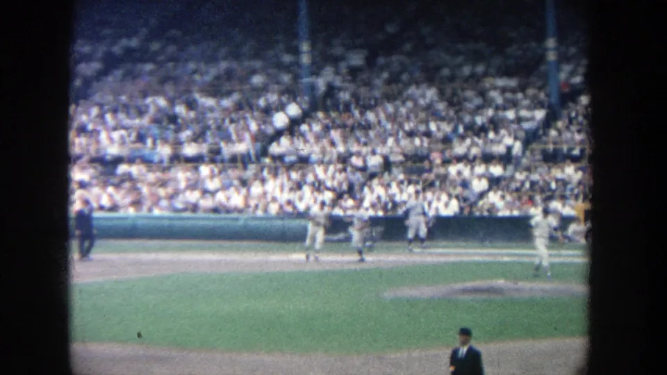 1964 8mm view of a baseball game at Yankee Stadium with players near the infield and a packed crowd behind them.