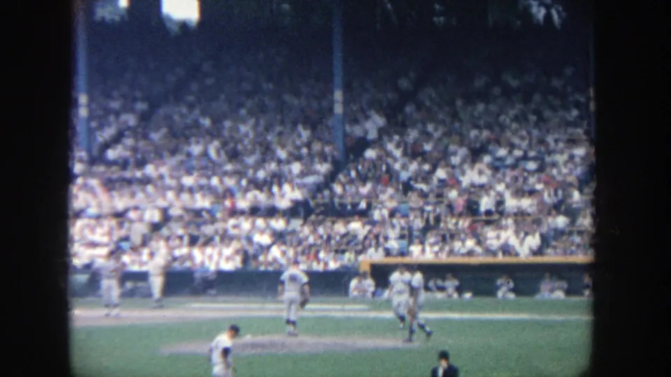 Home-movie view of a baseball play at Yankee Stadium, showing players near the infield and spectators packed into the stands.
