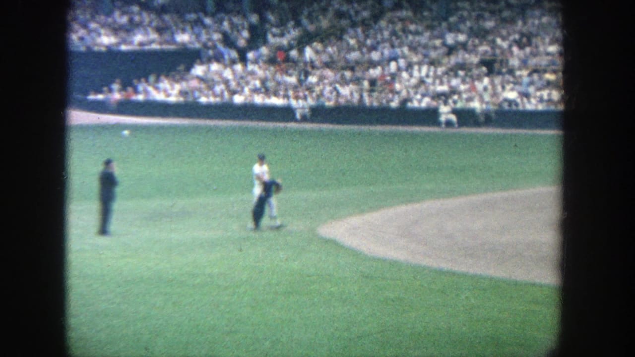 Baseball player on the infield grass near an official with crowd-filled stands behind.